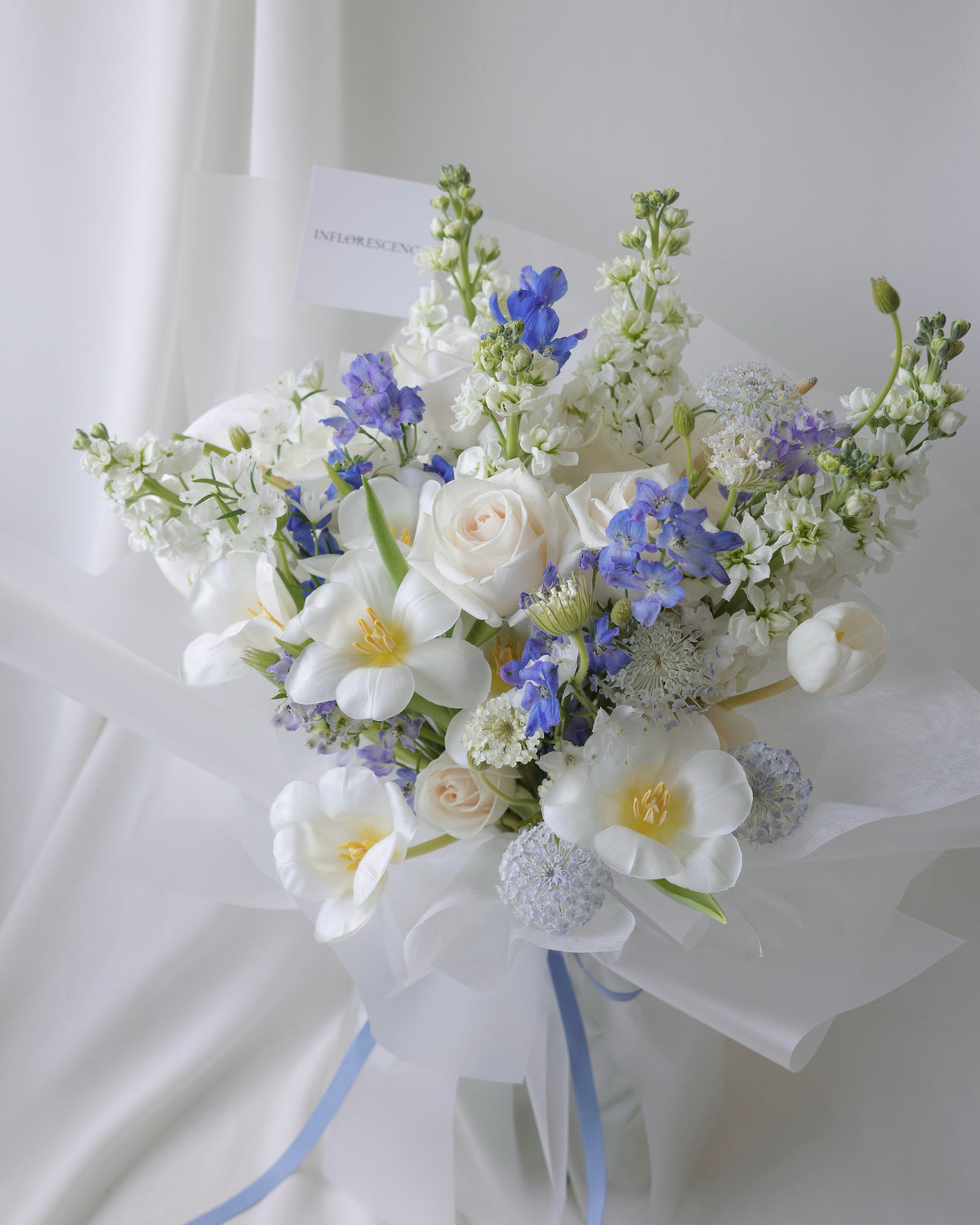 Elegant white and blue bouquet with delphiniums, tulips, and roses by Studio Inflorescence Singapore