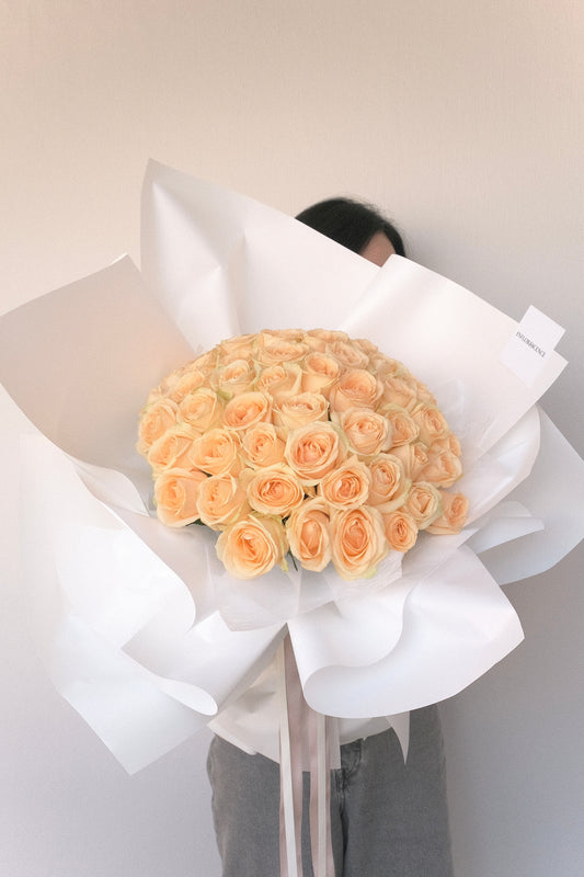 Champagne Rose Bouquet with 60 peach roses wrapped in white paper and satin ribbon
