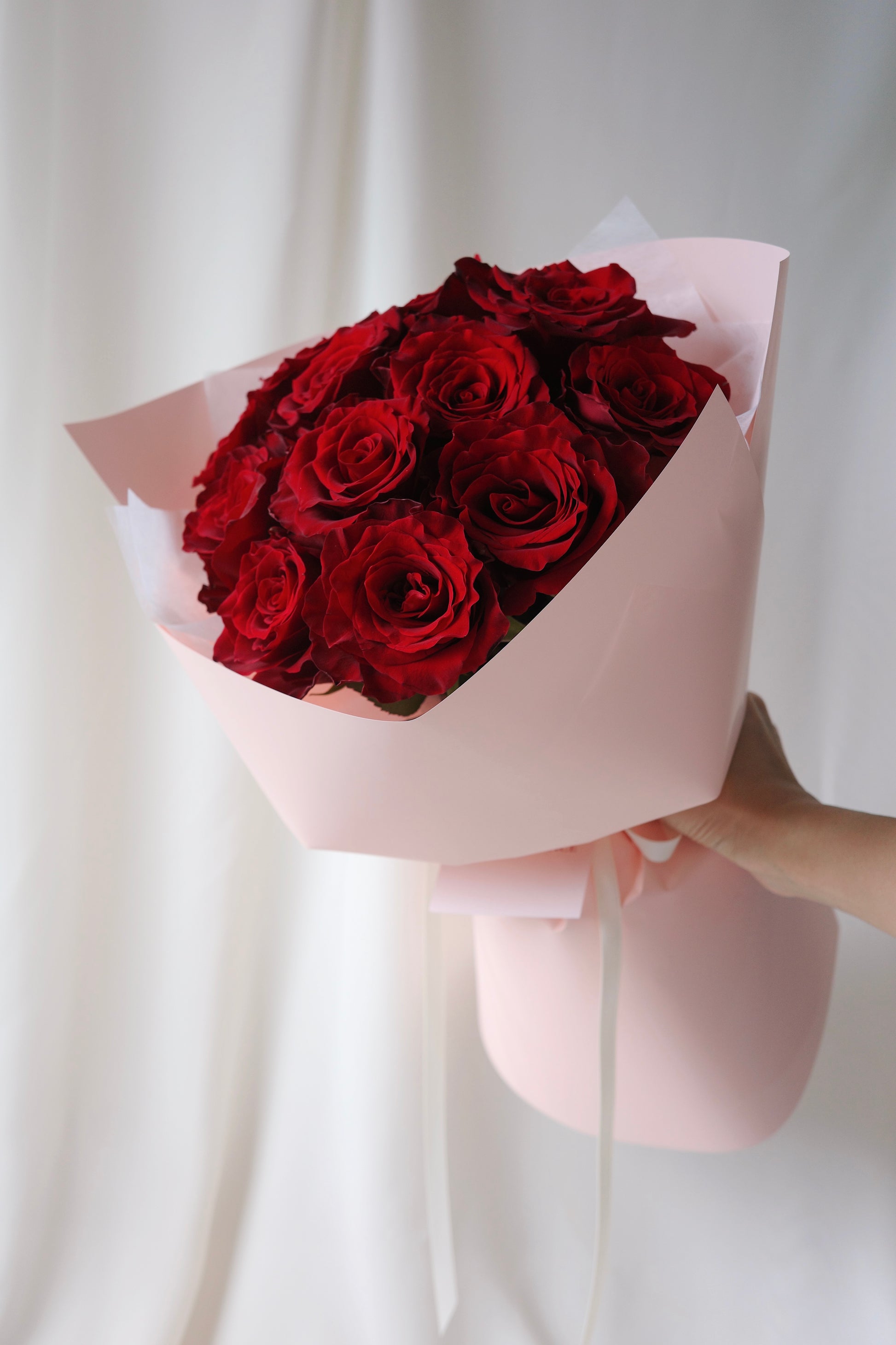 A dozen fresh red roses hand-tied in elegant blush pink wrapping, perfect romantic bouquet for anniversaries, birthdays, or Valentine’s Day.