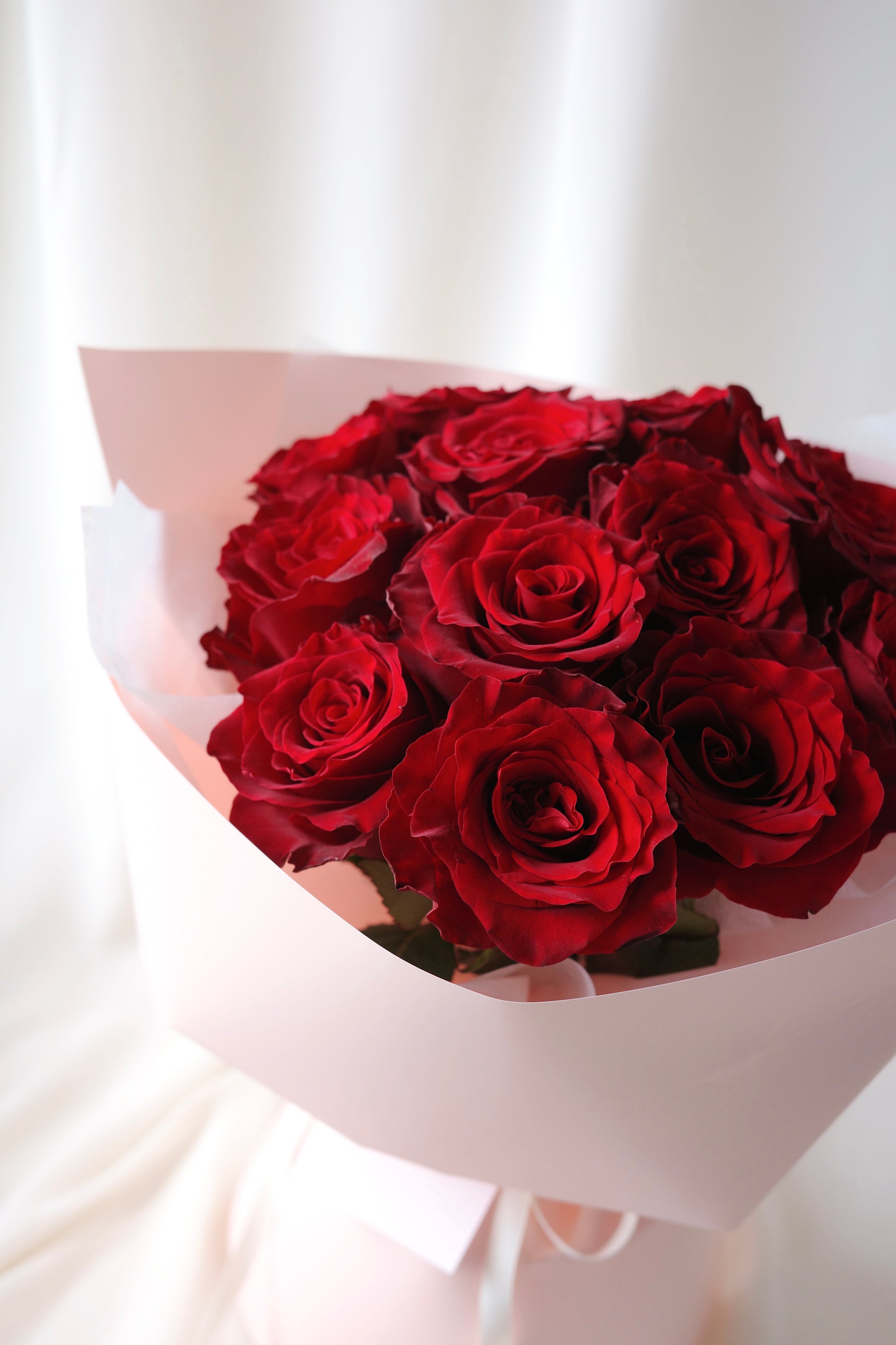 A dozen fresh red roses hand-tied in elegant blush pink wrapping, perfect romantic bouquet for anniversaries, birthdays, or Valentine’s Day.