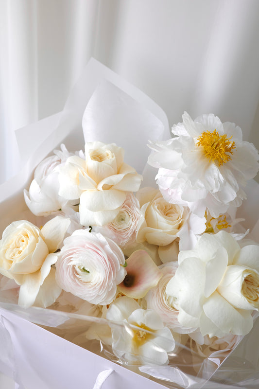 Elegant bouquet of soft yellow roses, white ranunculus, and soft blush flowers with delicate textures. A refined and romantic floral arrangement.