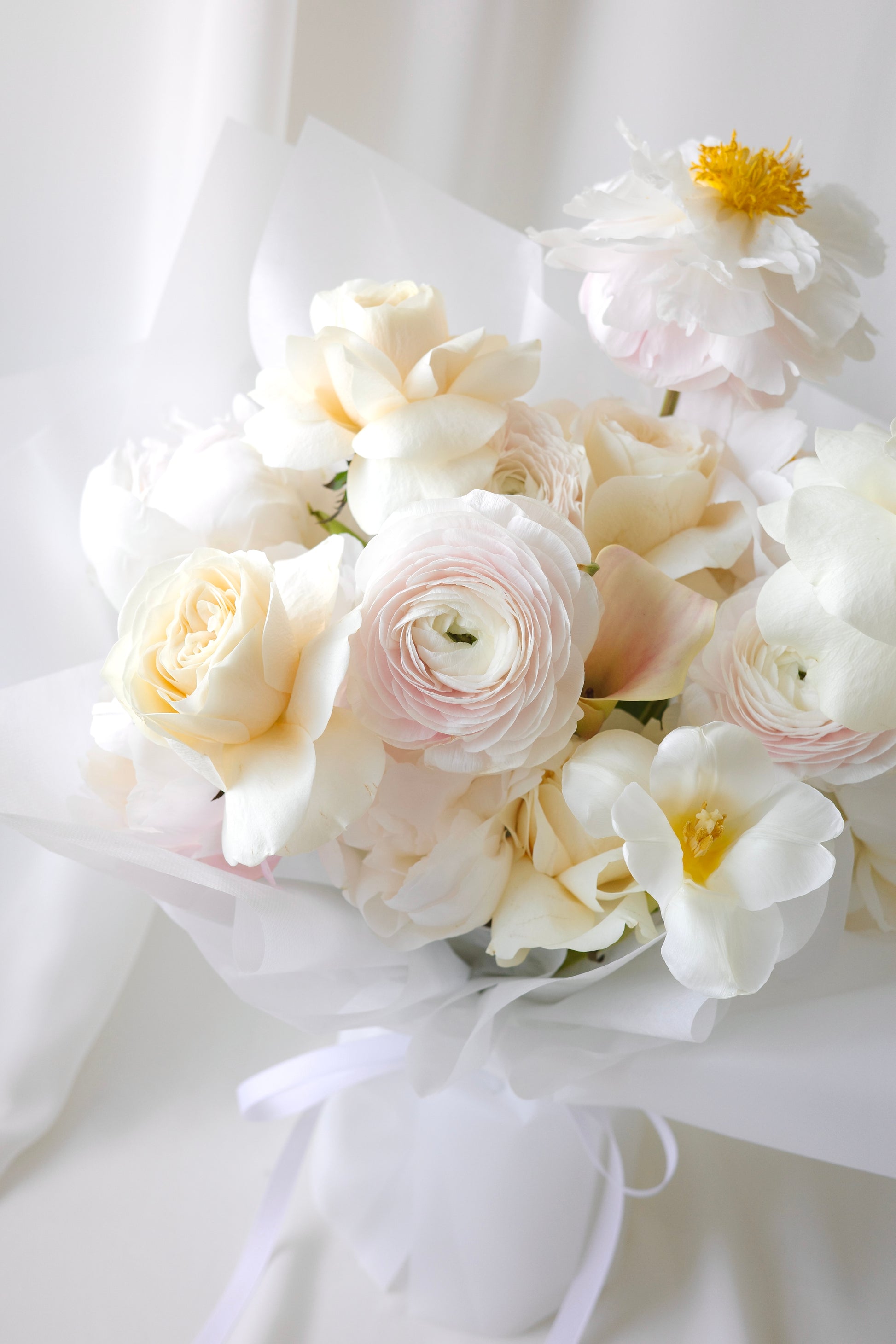 Elegant bouquet of soft yellow roses, white ranunculus, and soft blush flowers with delicate textures. A refined and romantic floral arrangement.