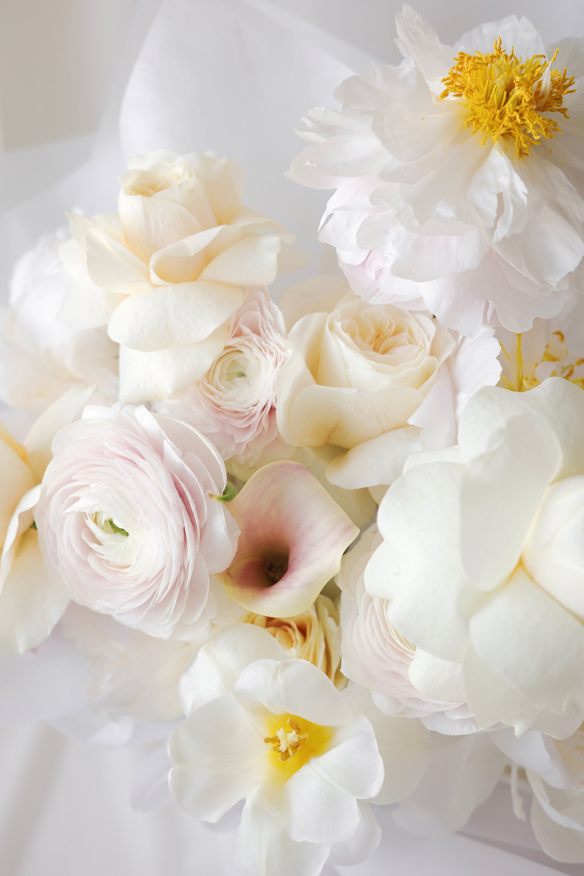 Elegant bouquet of soft yellow roses, white ranunculus, and soft blush flowers with delicate textures. A refined and romantic floral arrangement.