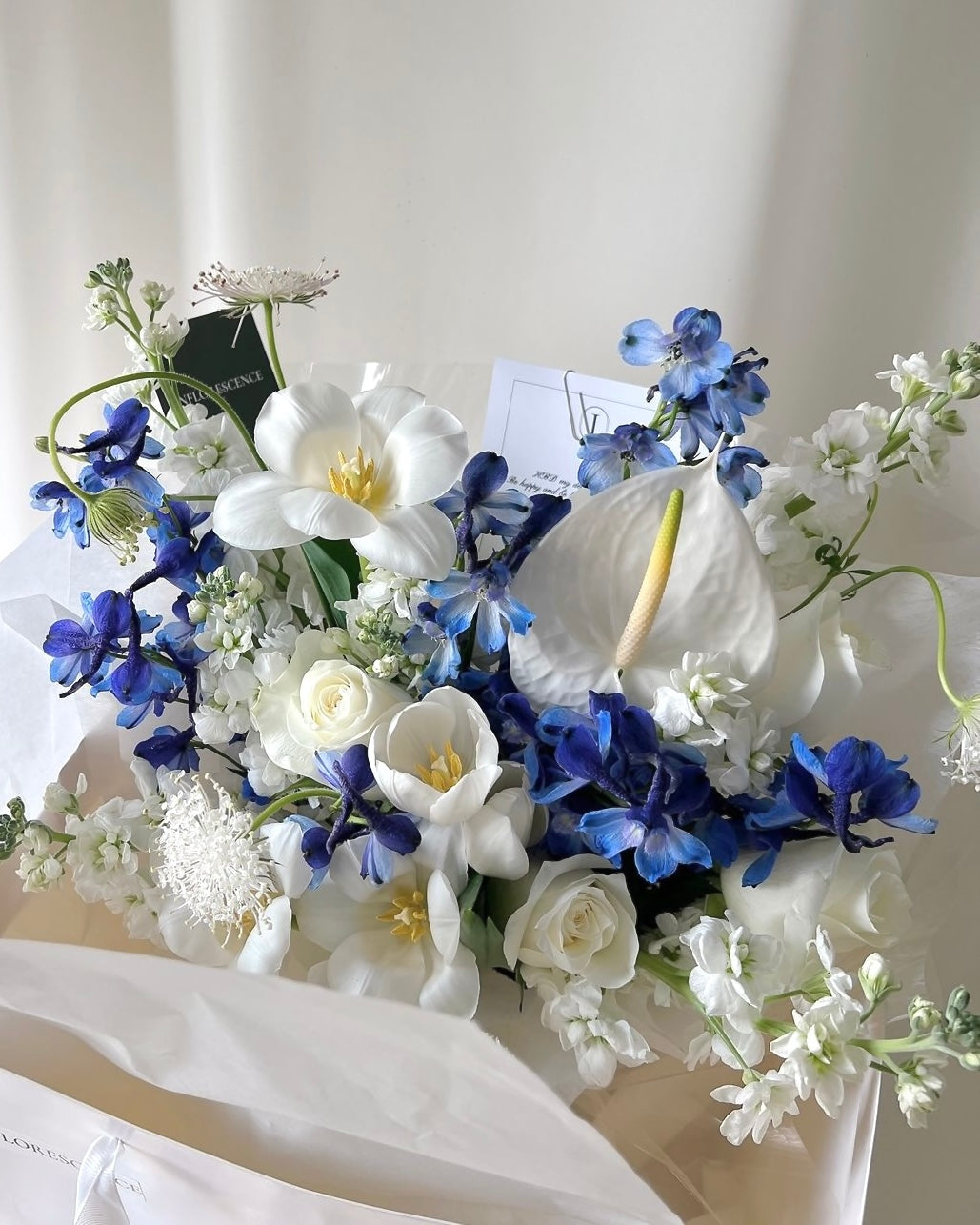Elegant white and blue bouquet with delphiniums, tulips, and roses by Studio Inflorescence Singapore