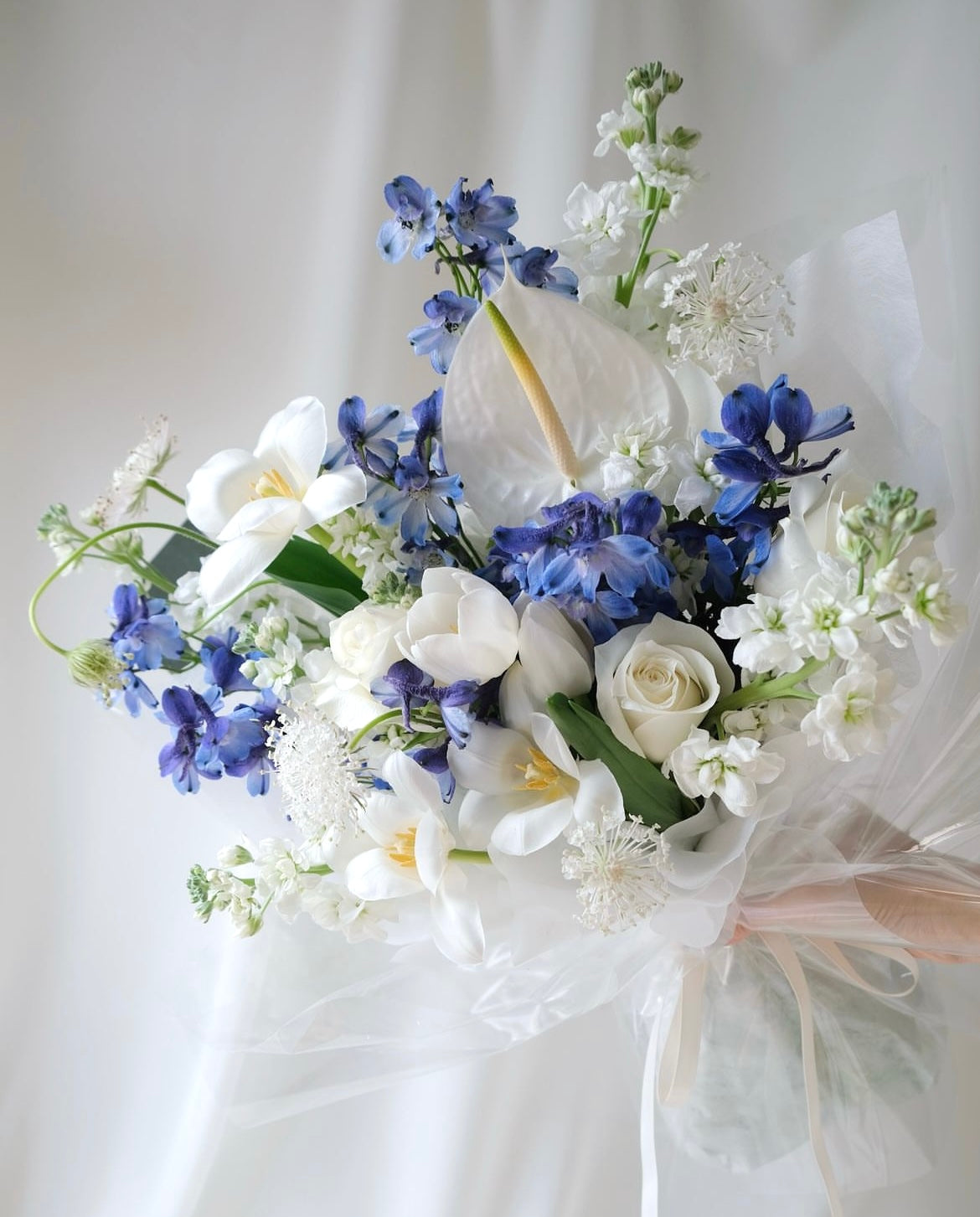 Elegant white and blue bouquet with delphiniums, tulips, and roses by Studio Inflorescence Singapore