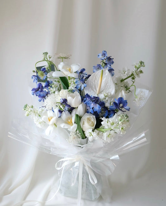 Elegant white and blue bouquet with delphiniums, tulips, and roses by Studio Inflorescence Singapore